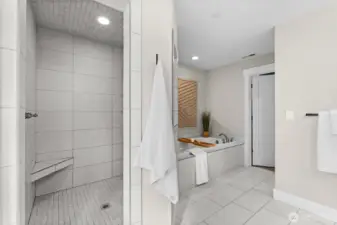 A large walk in fully tiled shower includes a shower chair and several built in shelves to hold all your shower essentials.
