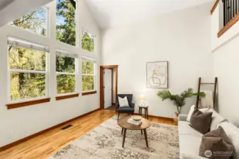 A dramatic wall of windows fills this living space with natural light, highlighting the home’s soaring ceilings. Surrounded by peaceful greenery, the view brings a sense of privacy and connection to the outdoors that’s hard to find.