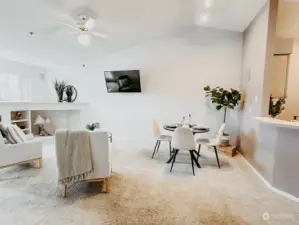 Bright and spacious living room with vaulted ceilings, a cozy wrap-around gas fireplace, and built-in surround sound for an inviting atmosphere.