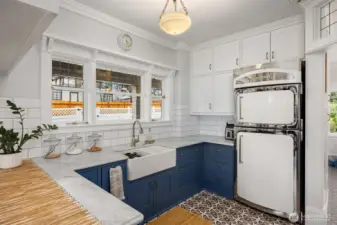 A study in both beauty and function, the “cold kitchen” offers a refined space dedicated to preparation, storage, and quiet morning rituals. Crisp white cabinetry rises to the ceiling, framed by classic millwork and period-inspired detailing, while deep navy lower cabinets ground the space with a rich, tailored contrast. Marble countertops and a farmhouse sink sit beneath a wall of divided-light windows, filling the room with soft, natural light.    The vintage-inspired refrigerator—both statement and conversation piece—anchors the room with timeless character, echoing the home’s historic roots while seamlessly blending with modern convenience. Thoughtfully designed for efficiency, this secondary kitchen allows the main entertaining spaces to remain pristine while supporting everyday living behind the scenes.    A rare and intentional feature, the dual “hot and cold kitchen” concept elevates both function and lifestyle—offering a level of sophistication seldom found, even in luxury hom