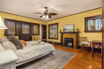 A serene primary bedroom offers warmth and comfort with hardwood floors, custom millwork, and a classic gas fireplace. Soft light and generous proportions create a peaceful retreat grounded in historic elegance with a huge deck!