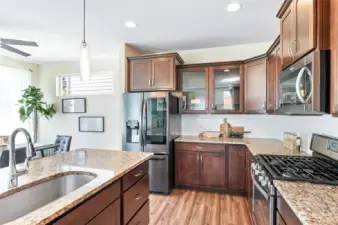 Open kitchen with glass panel cabinetry, granite countertops, full-height backsplash, and gas stove.