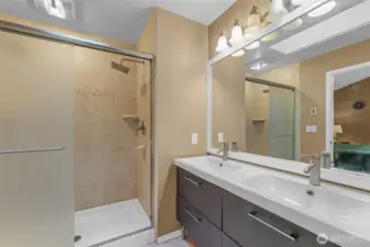 The private three-quarter en-suite bathroom features a dual-sink vanity with modern fixtures and an oversized mirror. The tiled walk-in shower includes an accent border and built-in shelf, offering both function and style.