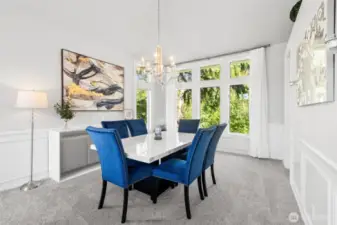 Bright & Sophisticated Dining Area - this light-filled formal dining room offers a stunning backdrop of lush greenery through expansive picture windows. The elegant chandelier, modern wall art, and rich blue seating create a stylish yet welcoming space for gatherings and everyday meals alike.