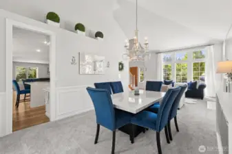Formal Dining & Living Room Combo - soaring vaulted ceilings and oversized windows flood this elegant formal dining and living area with natural light. Features a sparkling chandelier, wainscoting details, and plush carpet. A seamless layout perfect for entertaining or relaxing in style.