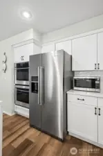 High-end Monogram double oven and KitchenAid stainless steel appliances complement the clean white cabinetry. Sleek finishes and abundant storage combine style and functionality in this gourmet kitchen.