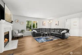 Cozy Family Room with Fireplace - spacious family room featuring a modern gas fireplace with marble surround, luxury vinyl plank flooring, and large picture windows that bring in natural light and garden views. Ideal for relaxing or hosting gatherings in comfort.