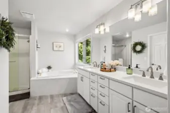 Bright and tranquil ensuite showcasing dual vanities, a large jetted soaking tub, and separate shower. Natural light pours in through the window, offering serene views and a luxurious atmosphere.
