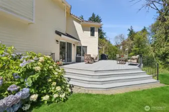 Backyard Retreat with Blooming Garden Beds. Step down into a beautifully landscaped yard featuring vibrant hydrangeas, a spacious deck, and a manicured lawn—ideal for play, gardening, or peaceful lounging.