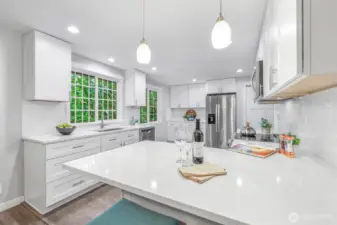 A closer view of the kitchen reveals an expansive island with seating, ideal for casual dining or conversation while cooking. The bright finishes and pendant lighting add a polished touch.