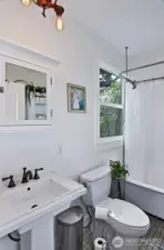 The full size bath on the main floor- Just around the corner from the kitchen. Tiled floors, porcelain vanity, clawfoot tub with a large window looking out the back yard, vintage lighting.