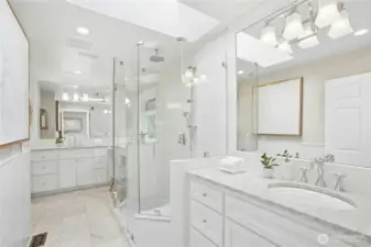 Spa-inspired retreat featuring heated floor, dual marble-topped vanities, frameless glass shower, and designer lighting beneath a skylit ceiling.