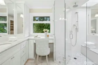 Natural light pours into this serene primary bath with marble surfaces, vanity seating, and tranquil views of the lake just outside.