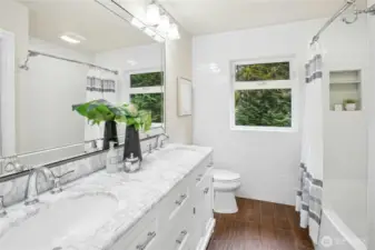 Start your day with ease at a marble-topped dual sink vanity framed by leafy views, beside a spa-like bath/shower with custom tile accents.