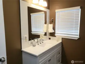 Close up view of the Main Guest Bath Room Showing New Vanity with Quartz Counter Top, Sink, Faucet, Paint, Mirror, 1 Inch Blinds and Tile Flooring.