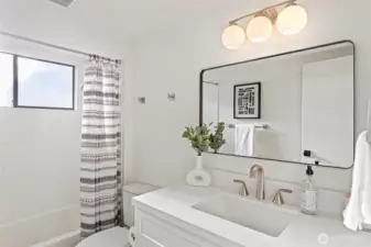 Full bathroom on main floor features new vanity and brushed nickel faucet, new lighting and mirror and bathtub with neutral white tile surround.