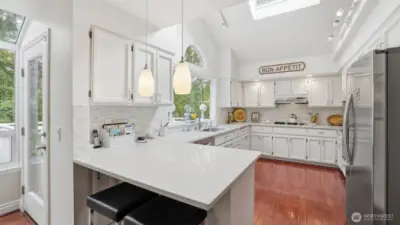 The kitchen is bright and open with white quartz counters white stacked tile backsplash, custom lighting and a large sky light as part of the vaulted ceiling. There is a garden window with a half round window above.  All the appliances remain with the home and all are Stainless steel.
