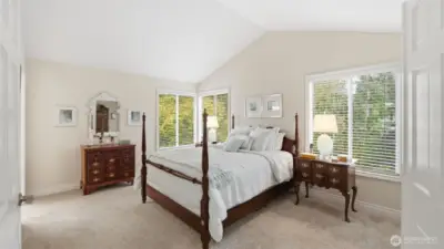Beautiful double doors open to the spacious primary suite.  A peaked ceiling amplifies the natural light that pours from the large windows.