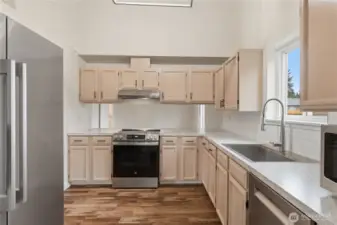 Bright and efficient kitchen with generous cabinetry, LVP flooring, and stainless steel appliances, highlighted by a window above the sink and an open bar to serve through.