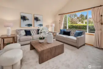 The bright living room boasts oversized windows framing lush greenery