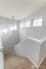 Light pours into this bright stairwell through a row of transom-style windows, highlighting clean lines, soft carpet underfoot, and a stylish hanging chandelier. It gives the entry a welcoming, open feel.