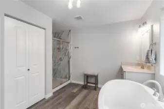 Another view of the primary bathroom showcasing the oversized walk-in shower with marble-style tile surround and glass doors. The layout offers plenty of open space and a clean, modern design that feels both luxurious and practical. There is also a huge linen closet for additional storage.