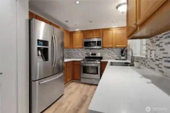 Functional galley-style kitchen featuring stainless steel double sink, all stainless appliances, sleek Corian countertops, and warm laminate wood flooring.  A pantry closet adds extra storage.