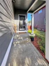 Nice front covered porch - perfect for holiday decorations. Wildflowers in the garden space give the entrance a nice pop of color and charm. Along with a maple tree and rhododendrons.
