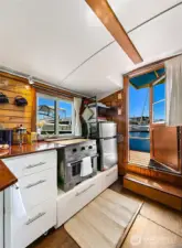 The galley pairs warm wood cabinetry with a propane Dickinson Marine Caribbean 2-burner stove/oven, efficient for daily cooking with a single 5-gallon tank lasting months — all framed by water views.