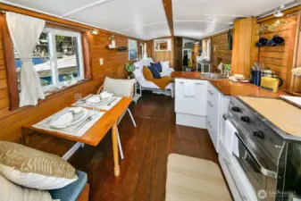 An open-plan galley and dining area runs the length of the saloon, featuring warm wood paneling, a Dickinson Marine Caribbean 2-burner propane stove/oven, and double-pane windows framing the lake just beyond.