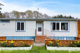 Charming front exterior with a welcoming entry, brick accents, and landscaped flower beds. The home’s clean lines and neutral tones enhance curb appeal in a serene country setting.
