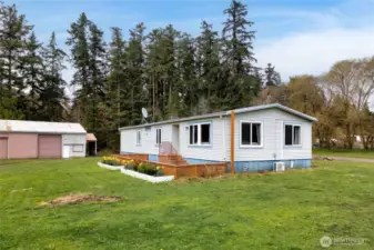 Charming single-level manufactured home set on spacious acreage, featuring a peaceful rural setting with mature trees and open green space. The property includes a large detached shop/garage, ideal for storage, hobbies, or equipment, offering the perfect blend of country living and functionality.