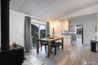 Inviting dining area with an open-concept layout, seamlessly connecting to the kitchen. Features include modern flooring, a cozy wood stove for added warmth, and sliding glass doors leading to a deck—perfect for indoor-outdoor living and entertaining.