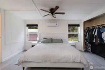 Spacious primary bedroom featuring a clean, modern aesthetic with neutral tones, luxury vinyl plank flooring, and abundant natural light. Includes a ceiling fan for comfort and a ductless mini-split system for efficient heating and cooling. Generous layout easily accommodates a king-size bed.