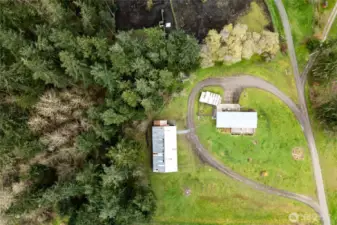 Aerial perspective showcasing the full layout of the property, including the home, detached shop, and additional outbuildings. The circular driveway and expansive yard highlight the functionality and space available.