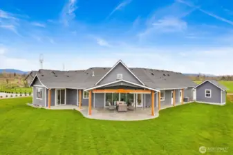Beautiful back view picture featuring the large, covered patio with stamped concrete and plumbed for an outdoor kitchen, gas fireplace, and hot tub. Sliders on the left lead to your primary ensuite.