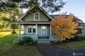 Spacious covered front porch a bit hidden with the colorful foliage.Another door just to right is entrance to the kitchen.