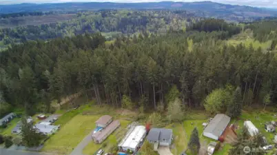 Stunning aerial view showcasing the home’s peaceful setting, backing to a lush forested greenbelt with sweeping territorial and mountain foothill vistas.