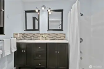 Bathroom with double vanity, solid surface counters, and tub/shower combination
