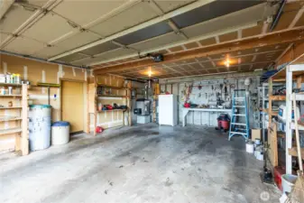 Spacious garage with extra refrigerator, workbench, and solid shelving