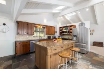 The expansive kitchen reflects woodland tones and textures from the surrounding landscaping, as reflected in the handsome granite countertops, pebble backsplash and rich, wood-stained cabinetry with display shelves.