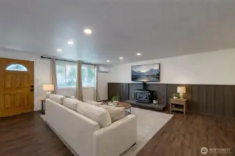 Great room features warm wood-style flooring, cozy woodstove, and mini-split. The photo is virtually staged.