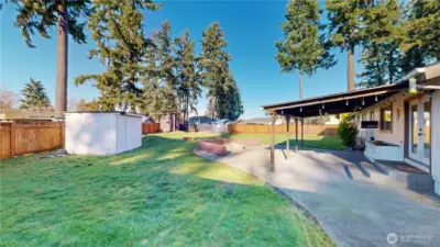 Fully fenced backyard offering a covered patio, firepit area, garden shed, and a playhouse.