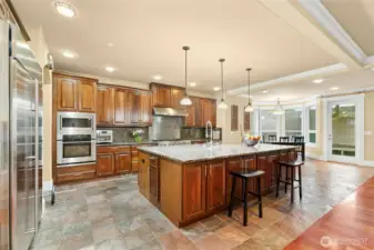 Chef’s kitchen featuring a Jen air 6-burner range with griddle, built-in GE Monogram refrigerator, wall oven and microwave, two Bosch dishwashers, beverage refrigerator, pot filler, and a built-in desk area.