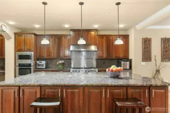 Chef’s kitchen featuring a Jen air 6-burner range with griddle, built-in GE Monogram refrigerator, wall oven and microwave, two Bosch dishwashers, beverage refrigerator, pot filler, and a built-in desk area.