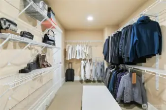Grand walk-in closet complete with a center bench and an additional dedicated shelving section, thoughtfully designed for maximum organization.