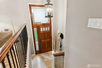 Entry features solid refinished stained wood door with sidelight and privacy glass portrait window above. Tiled landing leads to hardwood stairs with wood railing and wrought iron balusters.