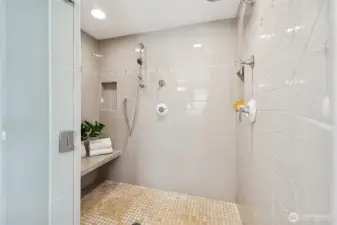Huge walk in shower has shower bench, tile floor and walls, multiple shower heads and tiled shower niche.