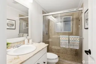 Downstairs 3/4 bath has tile floor, vanity with tile countertop and backsplash, tiled shower with glass enclosure and window with privacy glass.