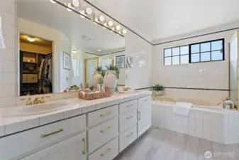 Peaceful en suite bathroom with dual sinks, new LVP flooring, newly painted cabinets, soaking tub, shower, and walk-in closet.